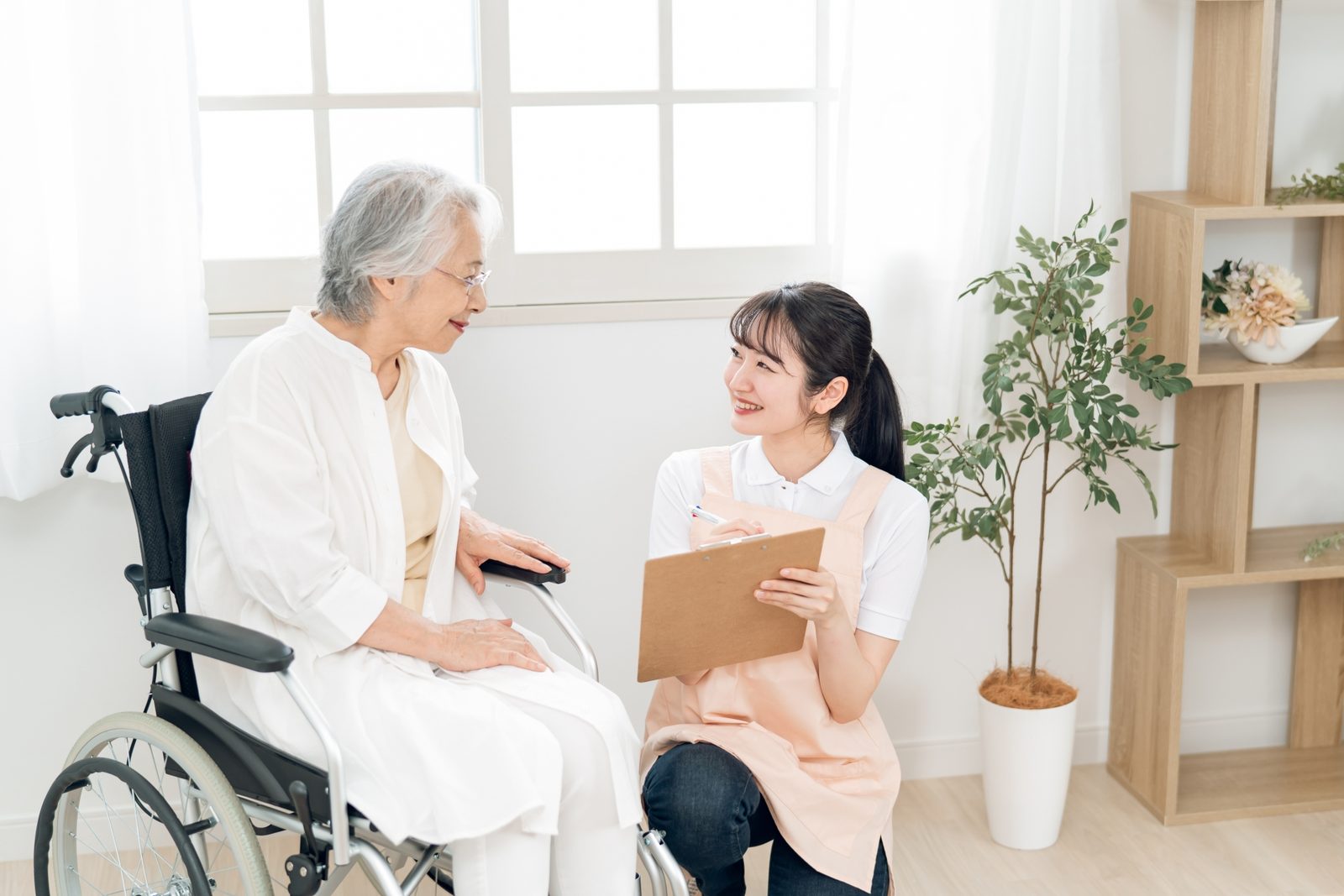 高齢女性の話を聞きながら記録する介護スタッフ