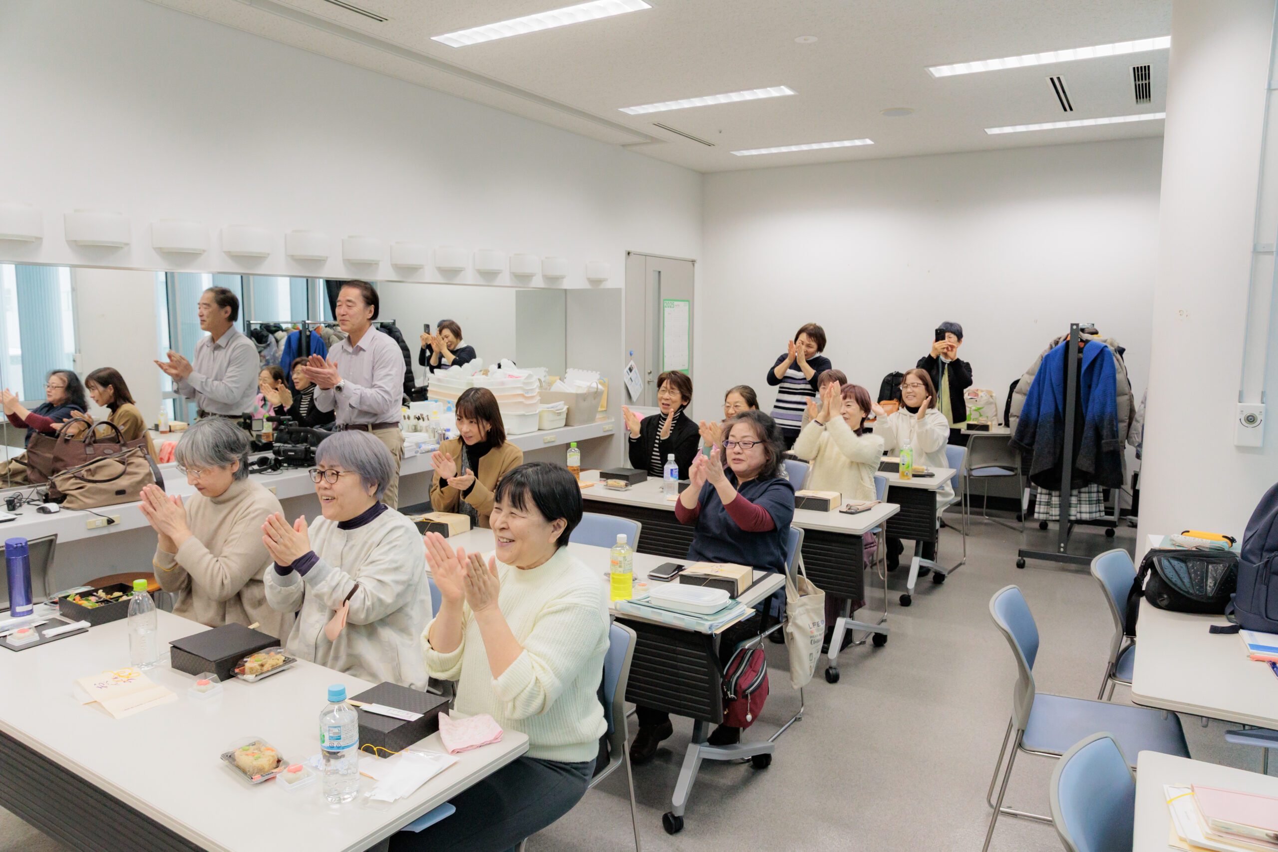 机を前に座り、拍手する参加者の様子