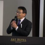 講演会でマイクを手に挨拶する折笠無我